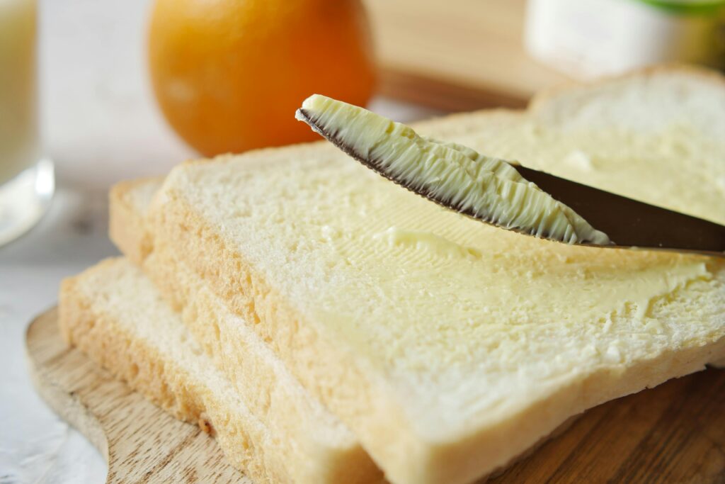 pexels photo 15703465 15703465 A close-up view of butter being spread on a slice of bread, perfect for breakfast scenes.