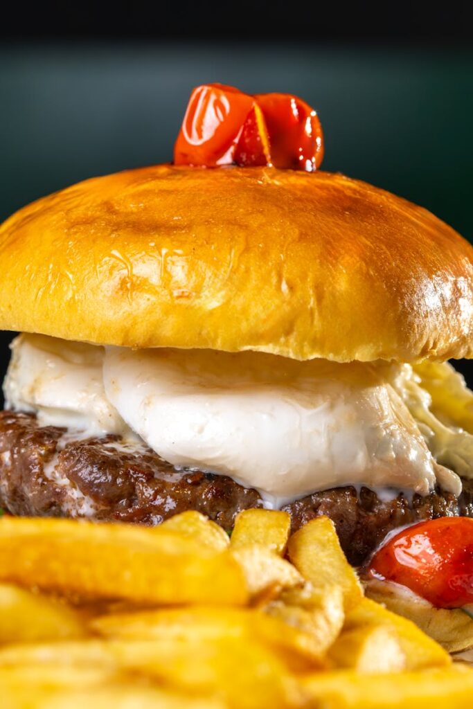 pexels photo 28841112 28841112 1 Delicious gourmet burger with melted cheese, fries, and cherry tomatoes on a plate.