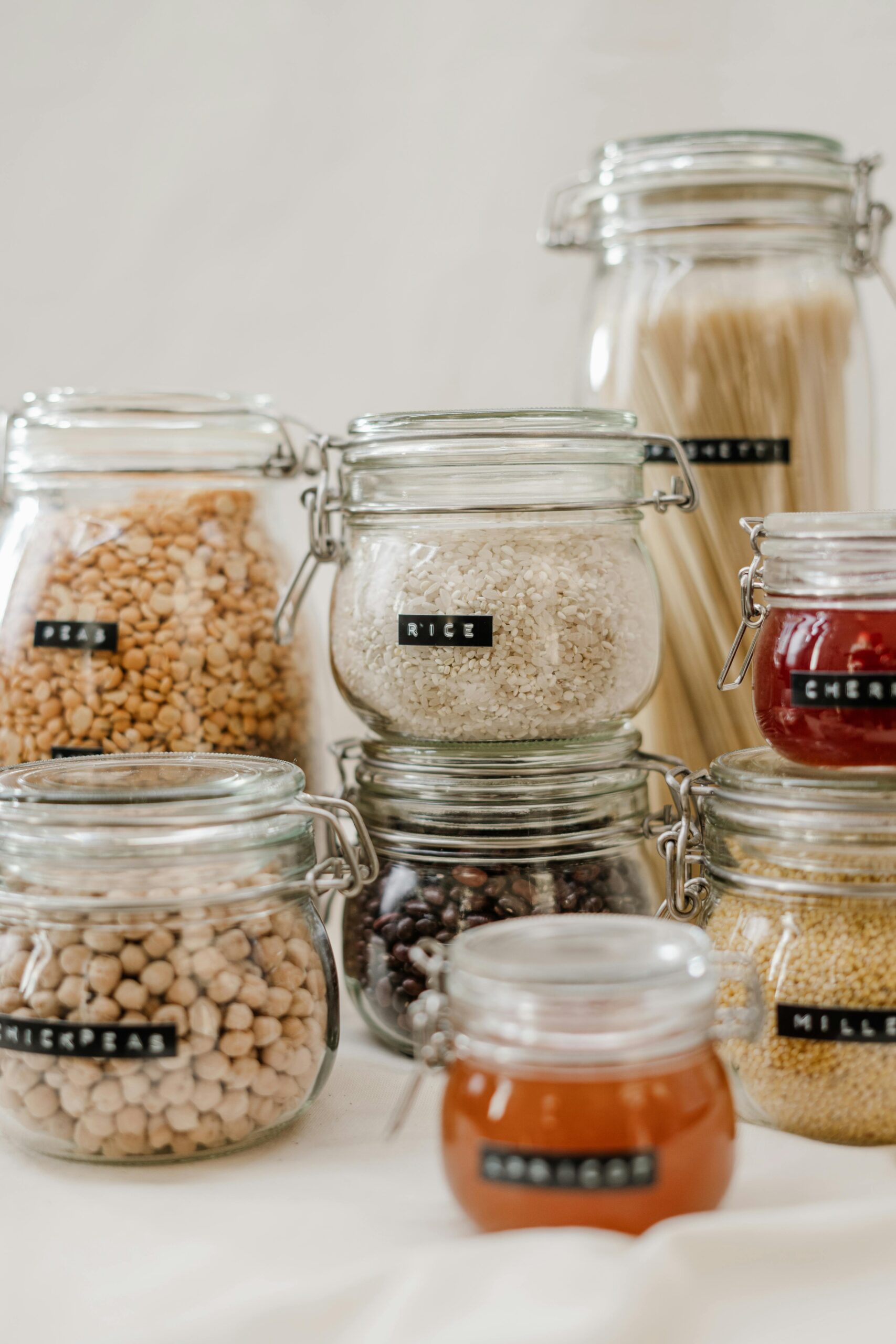 Glass jars filled with diverse kitchen ingredients like rice and chickpeas on a white background.